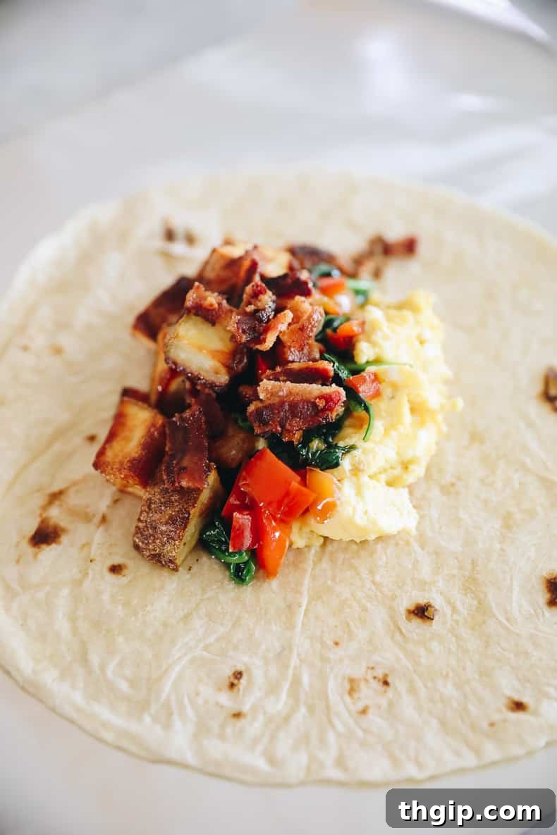 Grab-and-Go Frozen Breakfast Burritos 7 A large flour tortilla layered with scrambled eggs, bacon, potatoes, and spinach, ready to be wrapped into a breakfast burrito.