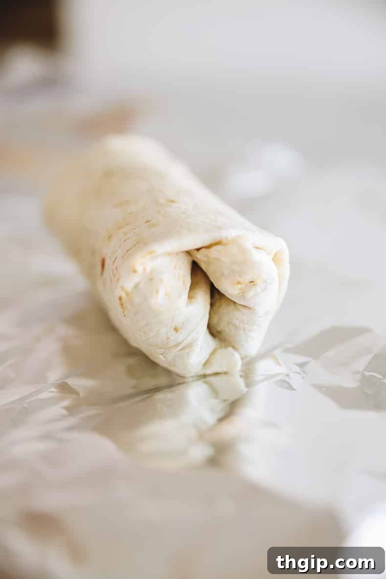 Grab-and-Go Frozen Breakfast Burritos 8 A perfectly wrapped breakfast burrito on a sheet of aluminum foil, ready for individual freezing.