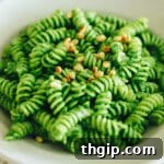 A vibrant bowl of kale pesto pasta, garnished with fresh herbs and cheese.