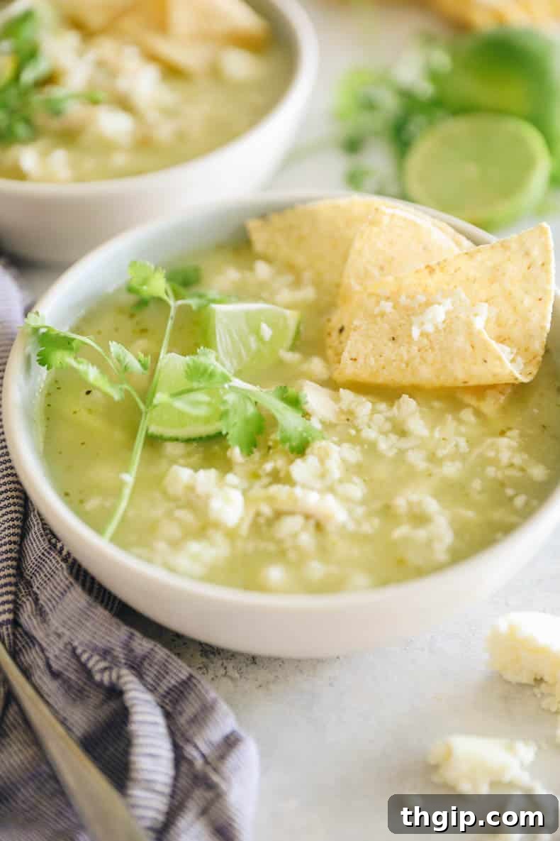 A steaming bowl of vibrant green chicken pozole, garnished with fresh cilantro and radish slices.