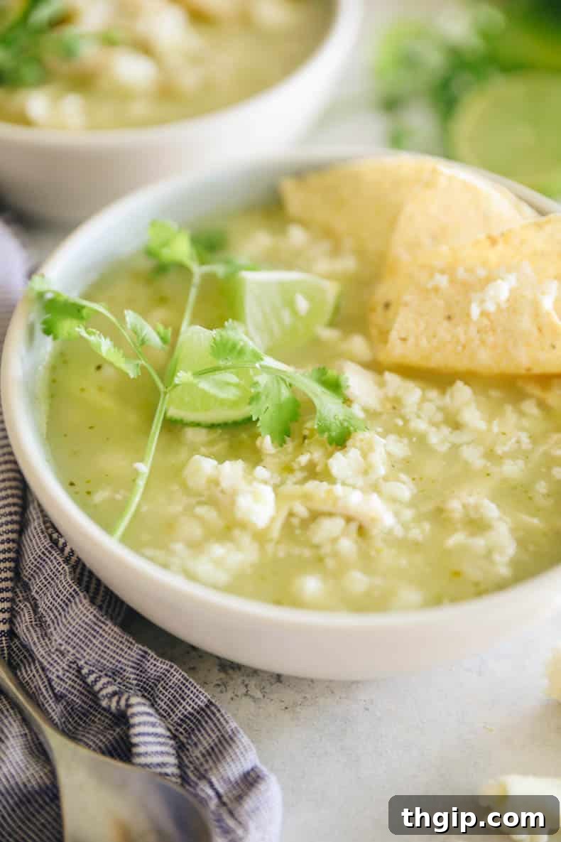 Close-up of a bowl of green chicken pozole, showcasing the rich broth, hominy, chicken, and fresh toppings.