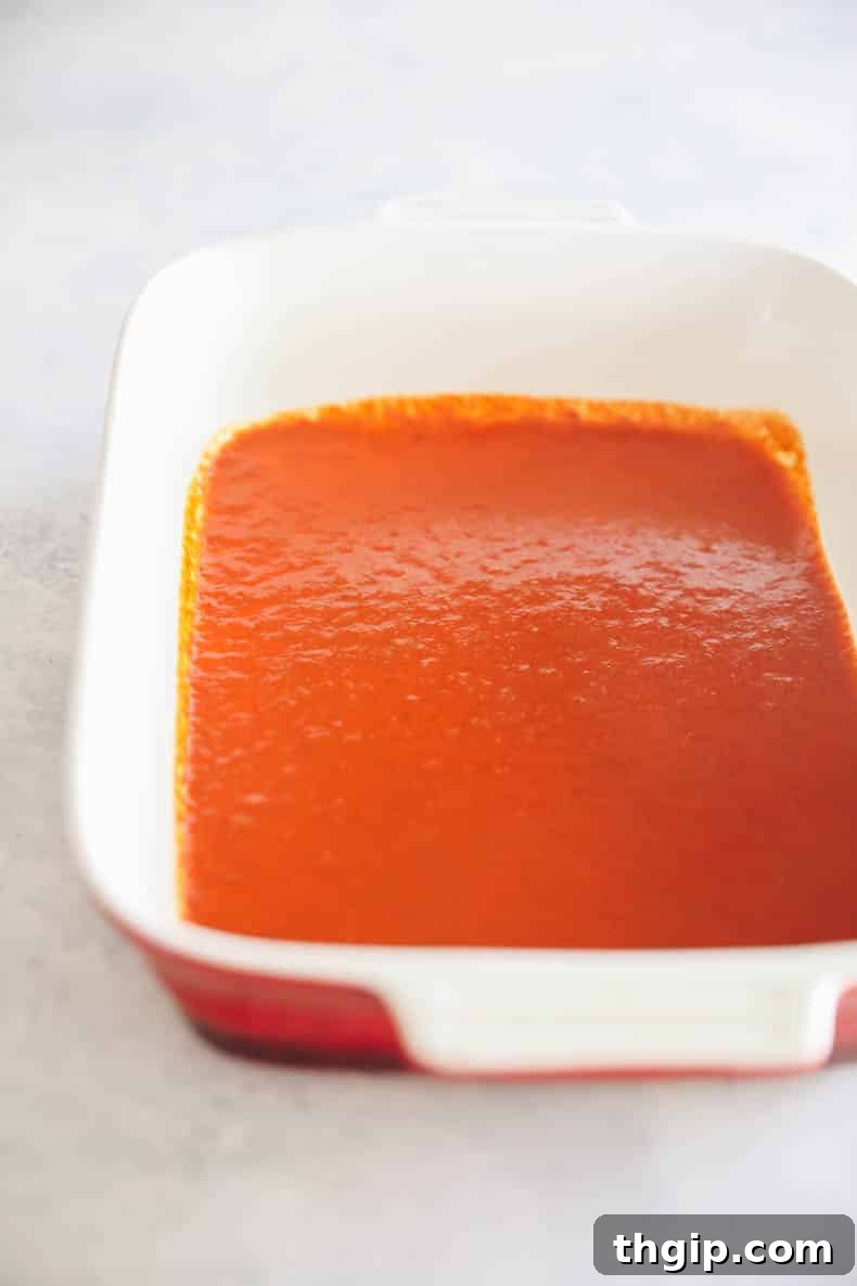 Zesty Black Bean Enchiladas 3 A vibrant red baking dish with a thin, even layer of red enchilada sauce spread across the bottom, ready for the filled tortillas.