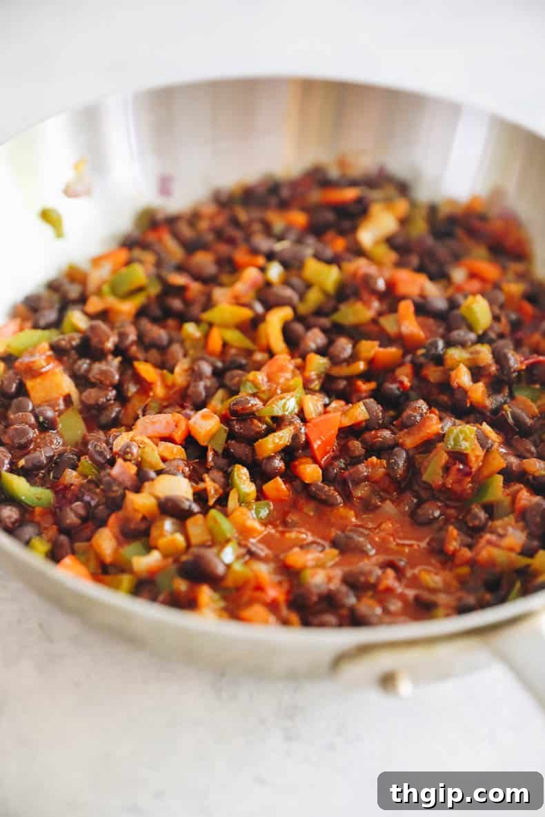 Zesty Black Bean Enchiladas 4 Close-up of a skillet filled with cooked black beans, sautéed bell peppers, and red onions, seasoned with spices, forming a rich and savory enchilada filling.