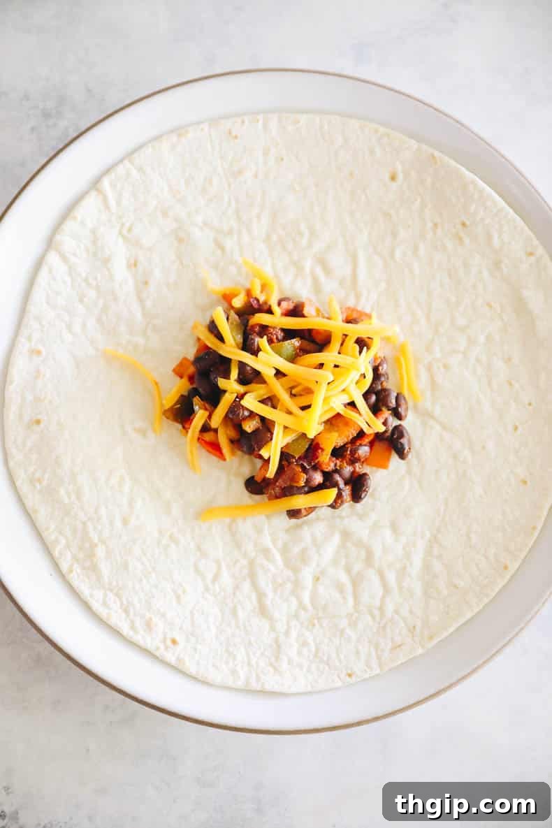 Zesty Black Bean Enchiladas 5 Close-up of a flour tortilla filled with black bean mixture and shredded cheese, expertly rolled and placed seam-side down in a baking dish, ready for baking.