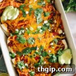 A close-up of a single golden-brown black bean enchilada, topped with vibrant cilantro and a dollop of sour cream, with other enchiladas blurred in the background.