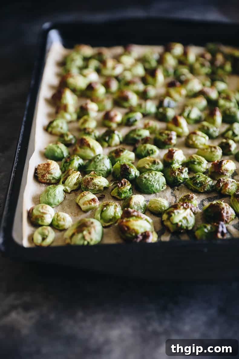 Partially roasted Brussels sprouts with a hint of balsamic on a sheet pan, showing early caramelization.