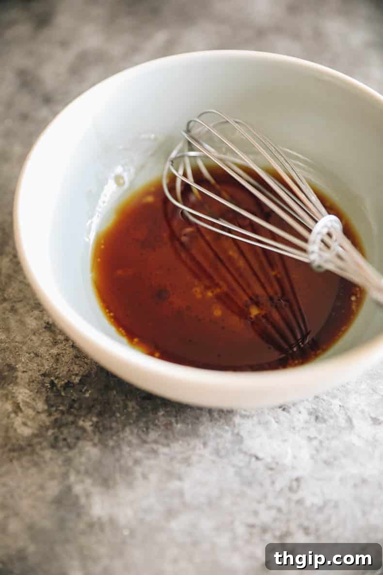 A small bowl containing a homemade balsamic glaze, with a whisk resting inside, ready for use.