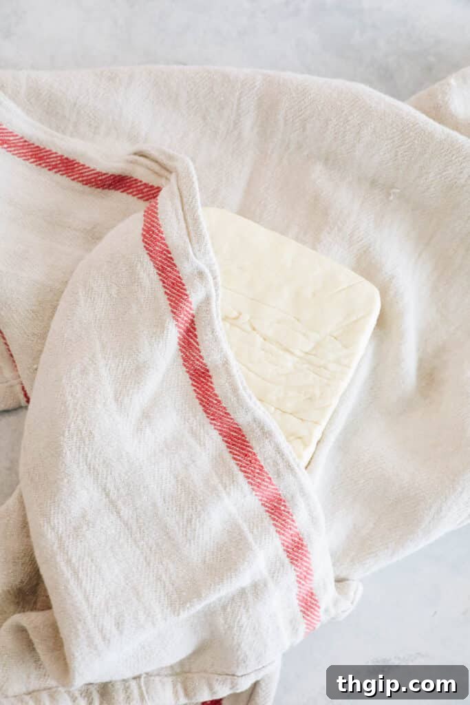 Savory Tofu Bolognese Pasta 3 A block of tofu being pressed between a dish towel and a heavy object to remove excess moisture.