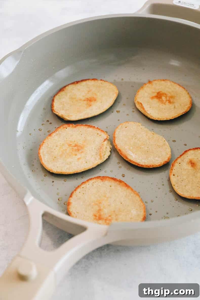 Miniature baby pancakes cooking in a skillet, showing bubbling batter and golden edges.