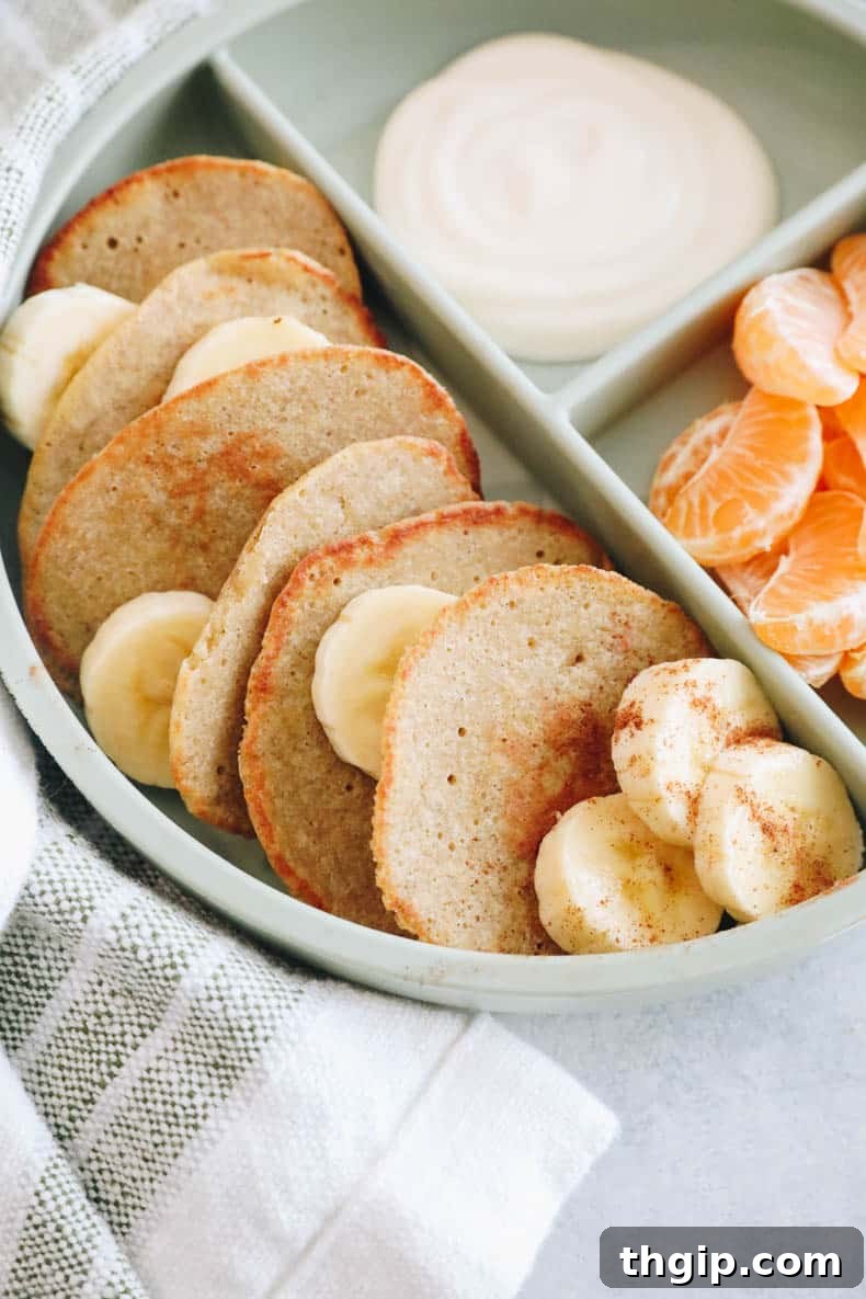 Plated baby banana pancakes in a green dish with orange slices and a dollop of yogurt on the side.