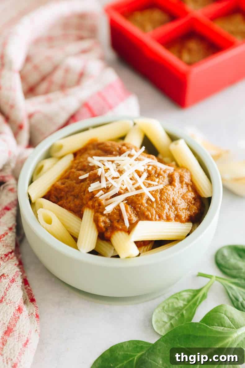 Secret Garden Pasta Sauce 2 Hidden veggie pasta sauce over penne noodles in a green kids bowl, garnished with a sprinkle of parmesan cheese and a fresh basil leaf.