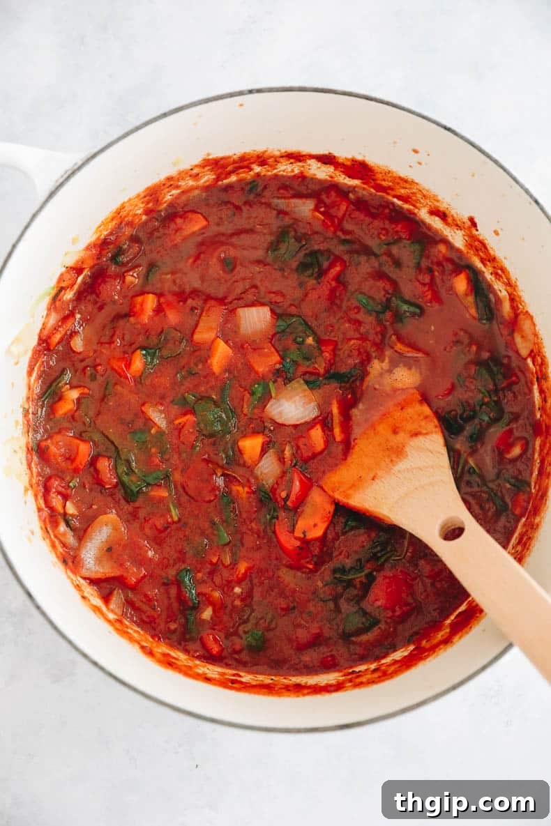 Secret Garden Pasta Sauce 5 Overhead shot of the pasta sauce for kids simmering in a white Dutch oven, with added tomatoes, herbs, and stock.
