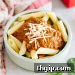 hidden veggie pasta sauce on penne pasta in a green kids bowl topped with parmesan cheese.