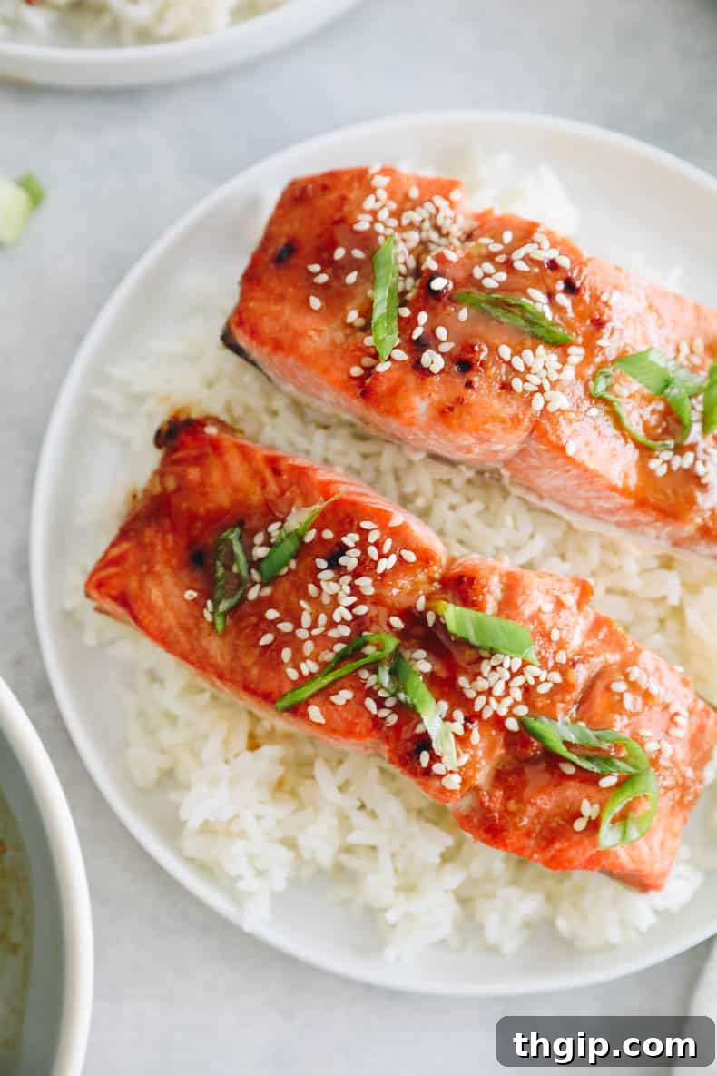 Effortless Miso Glazed Salmon 7 miso glazed salmon recipe on a bed of rice on a white plate. Salmon is sprinkled with sesame seeds and green onions.