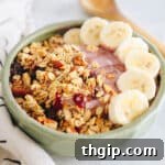 A beautifully presented pink smoothie bowl with fresh banana slices, granola, and a drizzle of honey, showcasing a delightful and nutritious breakfast.