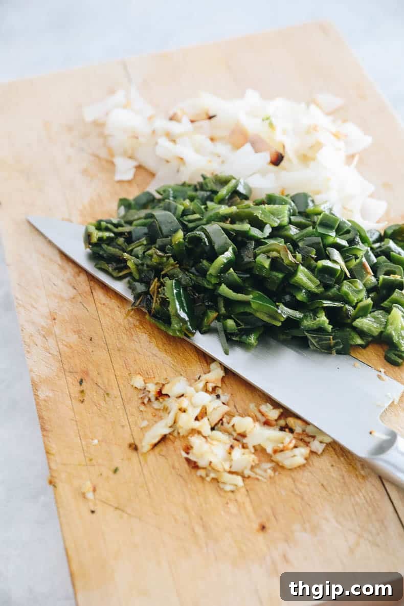 Cutting board showcasing perfectly chopped poblano peppers, jalapeno peppers, minced garlic, and diced onion after roasting, ready for the next step in the green chili recipe.