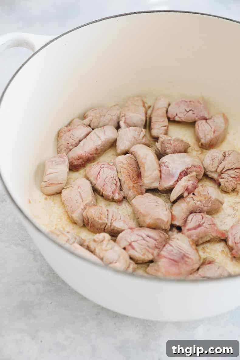 Close-up shot of pork tenderloin pieces browning evenly in a large cast-iron Dutch oven, achieving a golden crust that locks in flavor.