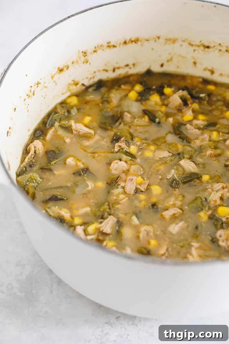 Rich and vibrant green chicken chili simmering in a large Dutch oven on the stovetop, bubbling gently as flavors meld and ingredients tenderize.