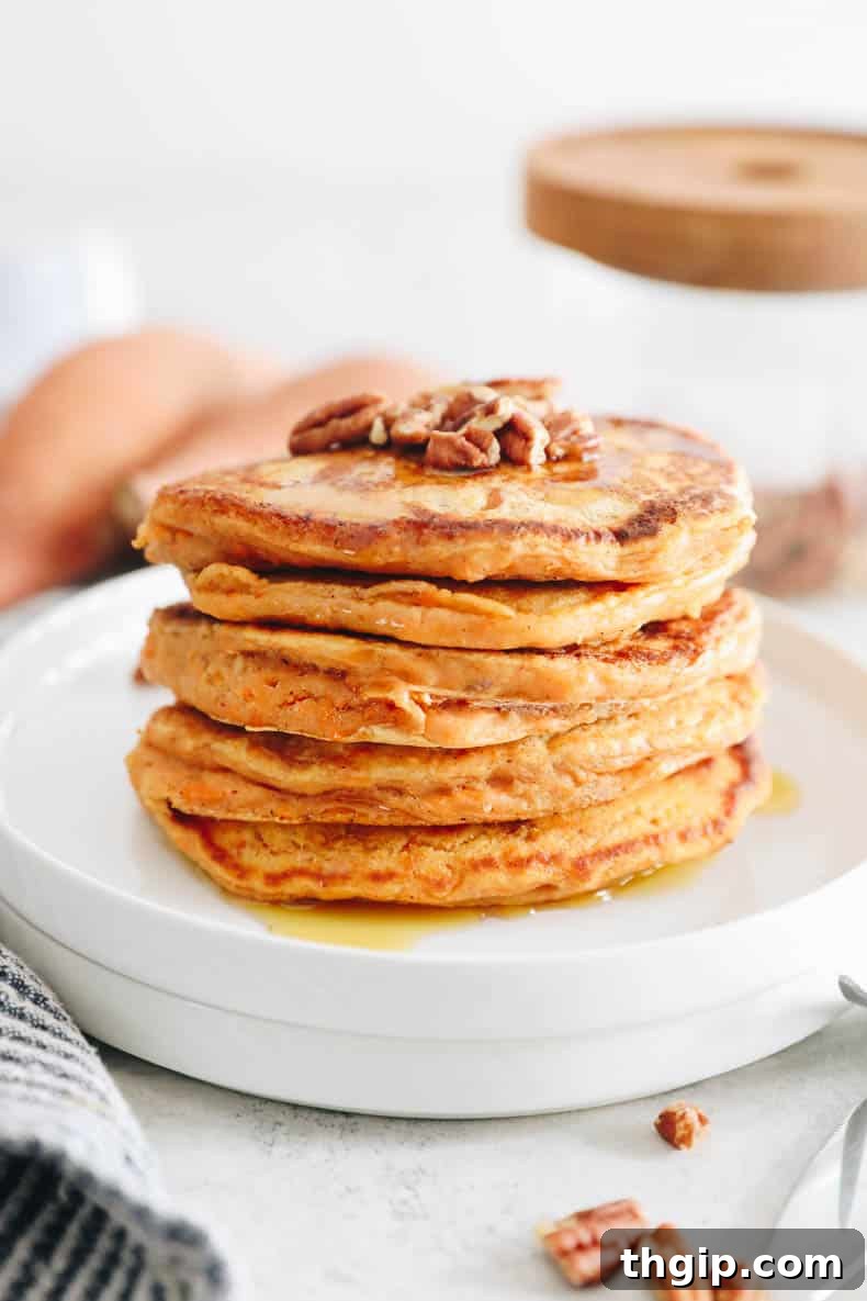 Golden Yam Griddlecakes 2 straight-on photograph of stacked sweet potato pancakes on a white plate. Topped with crushed pecans and maple syrup.