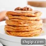stack of sweet potato pancakes topped with crushed pecans and maple syrup.