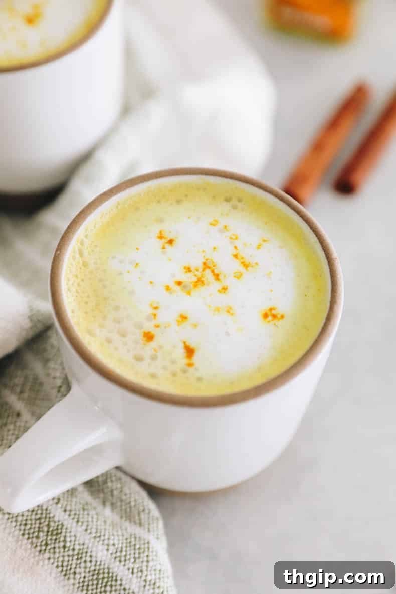Golden Turmeric Elixir 2 A beautifully frothed turmeric latte in a white mug, garnished with a light sprinkle of turmeric powder.