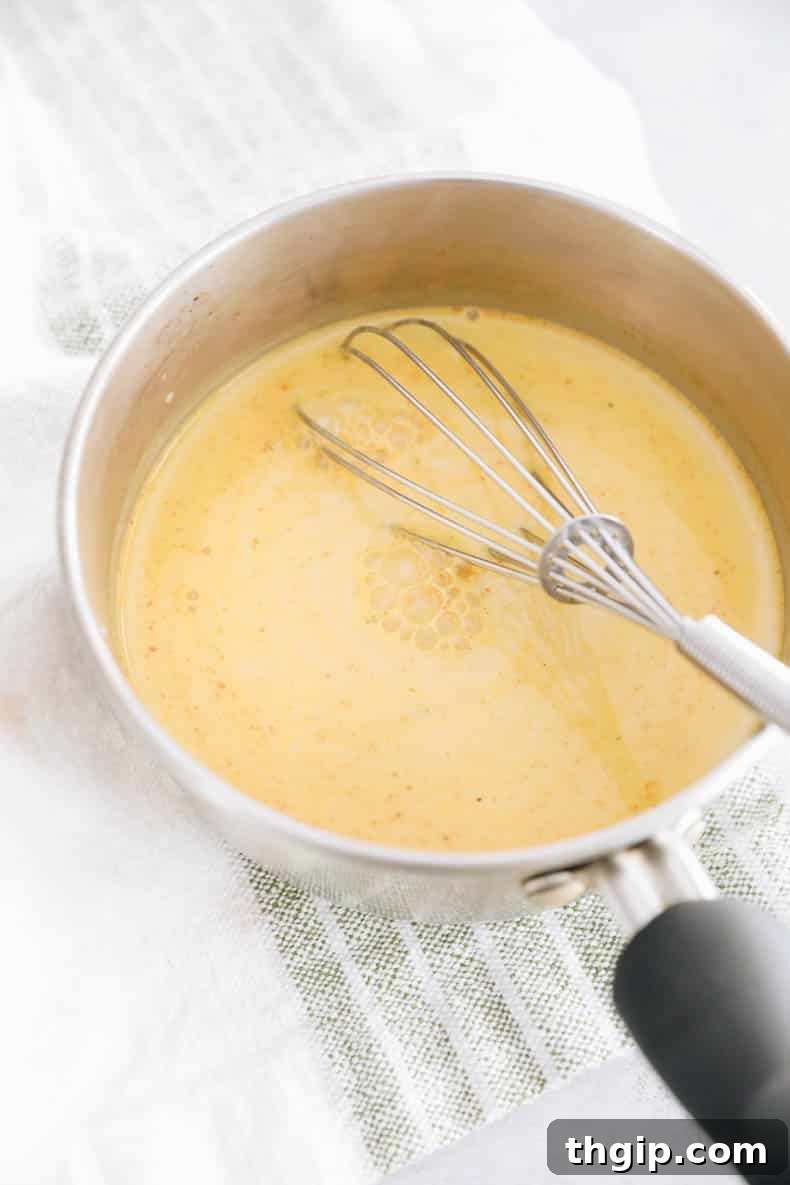 Golden Turmeric Elixir 3 Turmeric latte mixture being gently cooked in a small pot on the stove top, with a whisk ensuring a smooth consistency.