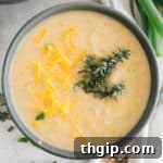 roasted cauliflower soup in a blue bowl topped with fresh thyme and cheddar cheese.