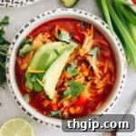 overhead shot of chicken enchilada soup in a white bowl topped with avocado, cheese and cilantro.
