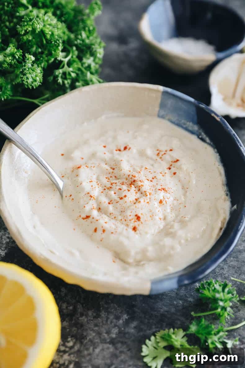 Vibrant tahini sauce presented in a elegant blue and white bowl, garnished with fresh lemon wedges and scattered parsley, showcasing its fresh and inviting appearance.