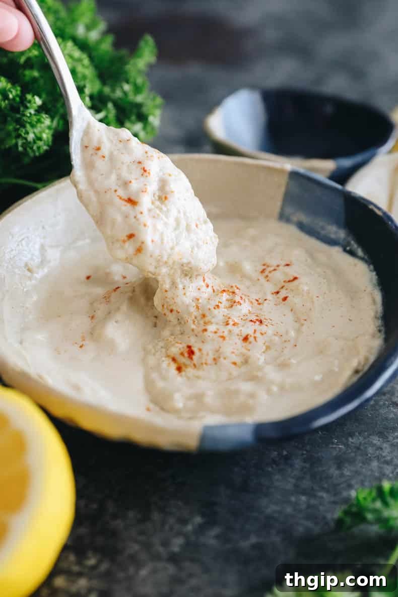 A spoon emerging from a bowl filled with freshly made tahini sauce, highlighting its creamy texture and inviting appeal.