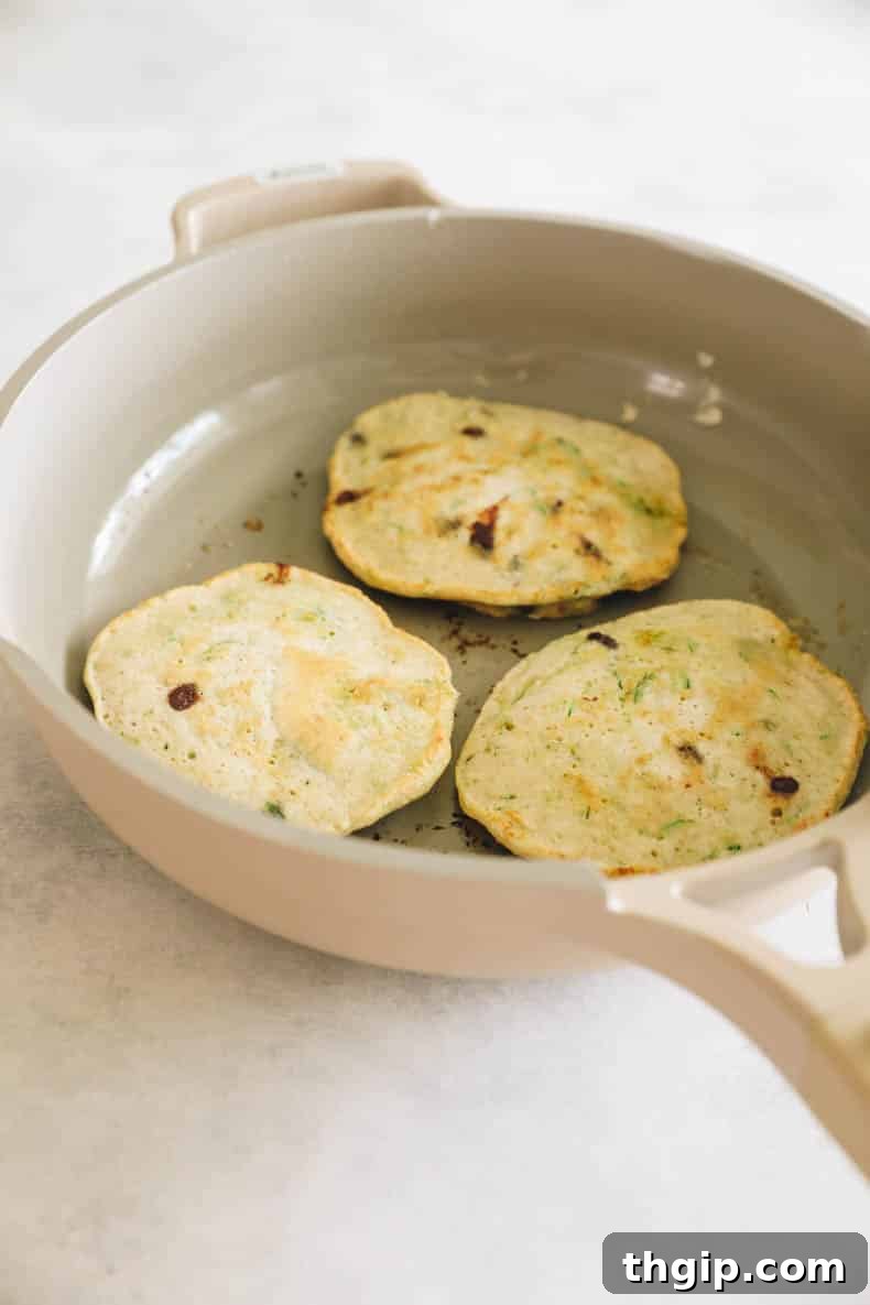 Golden brown zucchini pancakes cooking in a non-stick pan.