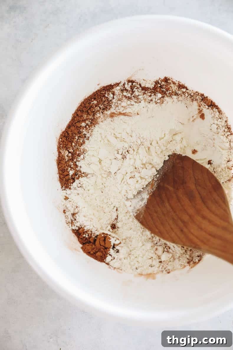 Zesty Zucchini Brownies 5 A large white mixing bowl holds the carefully combined dry ingredients for zucchini brownies, showing a uniform blend of flour, cocoa, and other powders.