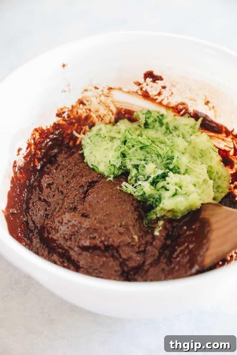Zesty Zucchini Brownies 6 A rich, dark brownie batter is seen in a bowl, with flecks of shredded zucchini visible, demonstrating the thorough but gentle incorporation of ingredients.