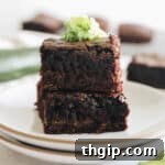 Stacked zucchini brownies on a white plate, garnished with fresh grated zucchini, showcasing their rich texture and healthy secret.