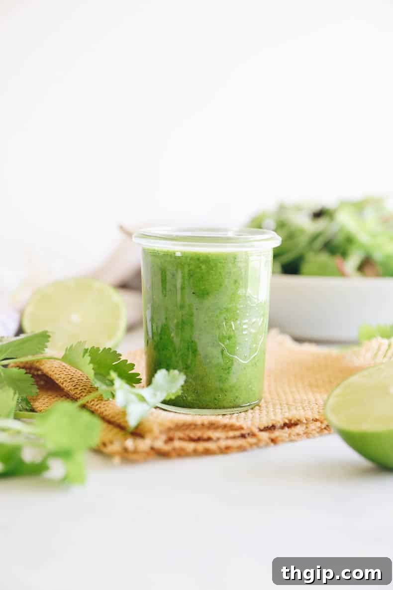 Vibrant Cilantro Lime Dressing 5 Close-up of vibrant cilantro lime dressing in a small mason jar, with a fresh green salad blurred in the background, showcasing its perfect pairing.