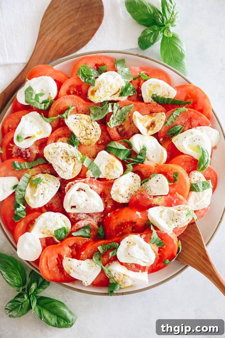 A vibrant tomato burrata salad displayed on a large platter, generously drizzled with premium olive oil and aged balsamic glaze, ready to be served.