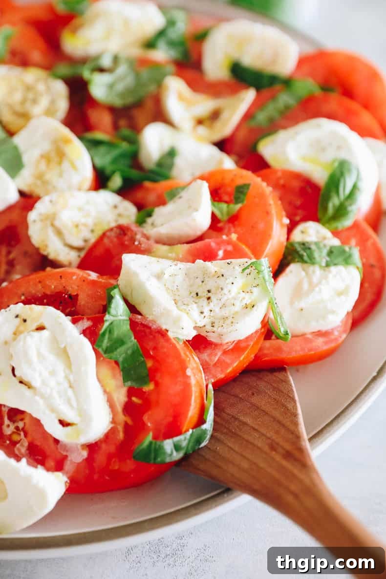 The final step in making burrata salad, with olive oil and balsamic vinegar being drizzled over the arranged tomatoes and burrata, seasoned with salt and pepper.