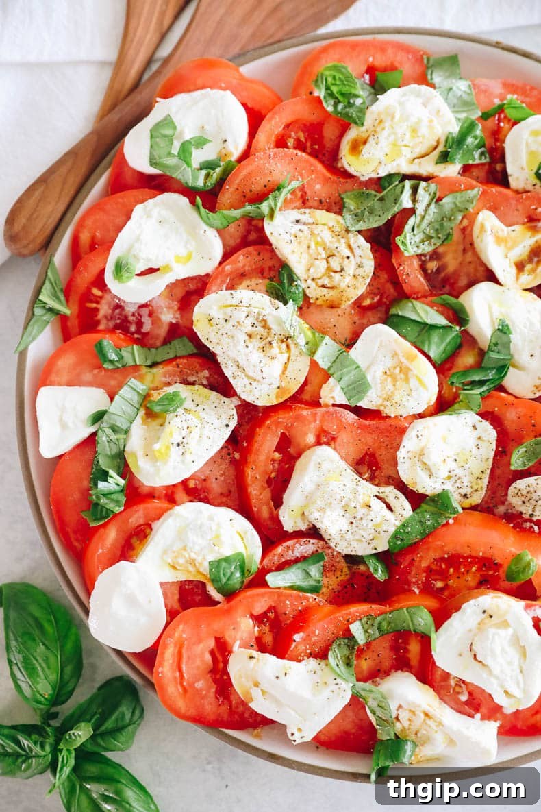 Close-up of a delightful tomato burrata salad, garnished with fresh basil, glistening with olive oil, and seasoned with salt and pepper.