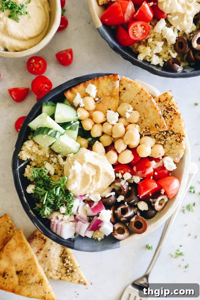 An inviting overhead photo of a colorful Mediterranean bowl featuring fluffy quinoa, briny Kalamata olives, crumbled feta, crisp pita chips, creamy hummus, juicy cherry tomatoes, and thinly sliced red onion.