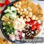 overhead photo of a mediterranean quinoa bowl with pita chips, hummus, tomatoes, cucumbers, red onion and olives.