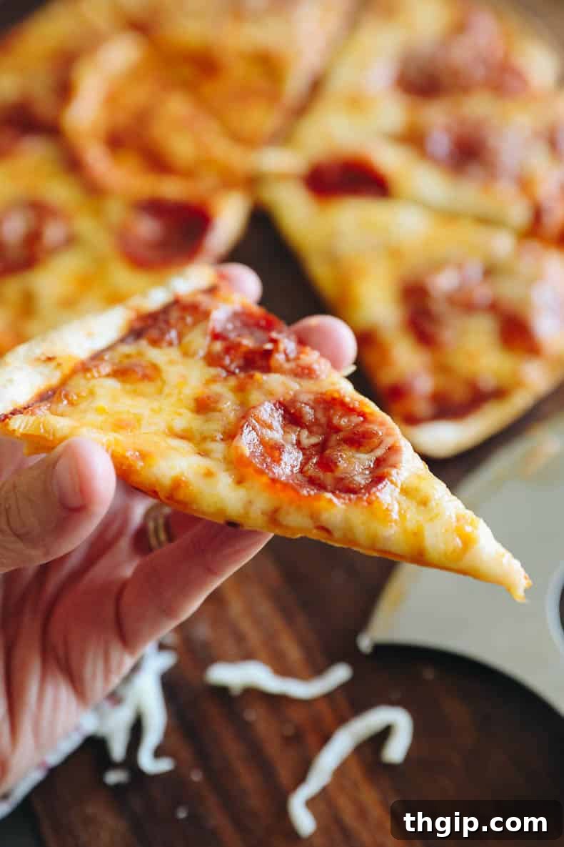 Crispy Tortilla Pizza 5 A hand holding a slice of crispy pepperoni tortilla pizza.