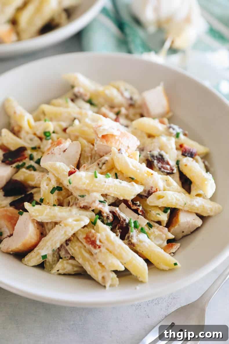 A shallow white bowl filled with creamy chicken bacon ranch pasta, garnished with fresh chives, showcasing the tender chicken, crispy bacon, and rich sauce.