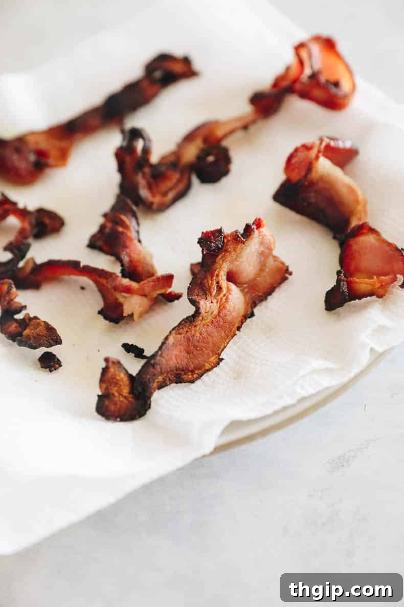 Crispy strips of bacon cooling and draining on a plate lined with paper towels after being perfectly cooked, ready to be chopped for the pasta dish.