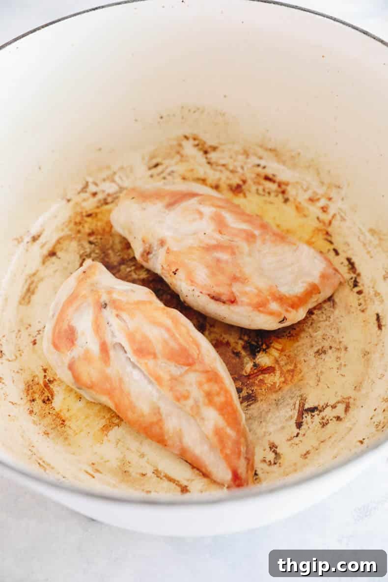 Juicy boneless, skinless chicken breasts perfectly cooked and resting in a large Dutch oven, preparing to be chopped for the creamy pasta.