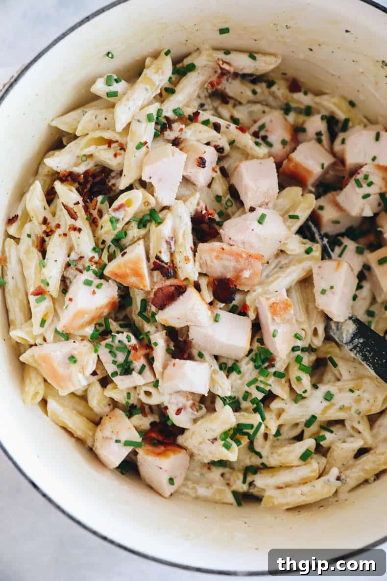 A vibrant overhead shot of the creamy chicken bacon ranch pasta in a large pot, garnished generously with fresh green chives, highlighting its rich texture and appetizing appeal.