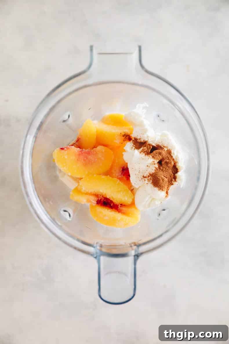 A selection of fresh and frozen peach smoothie ingredients, including sliced peaches, a banana, and milk, arranged around a high-speed blender.