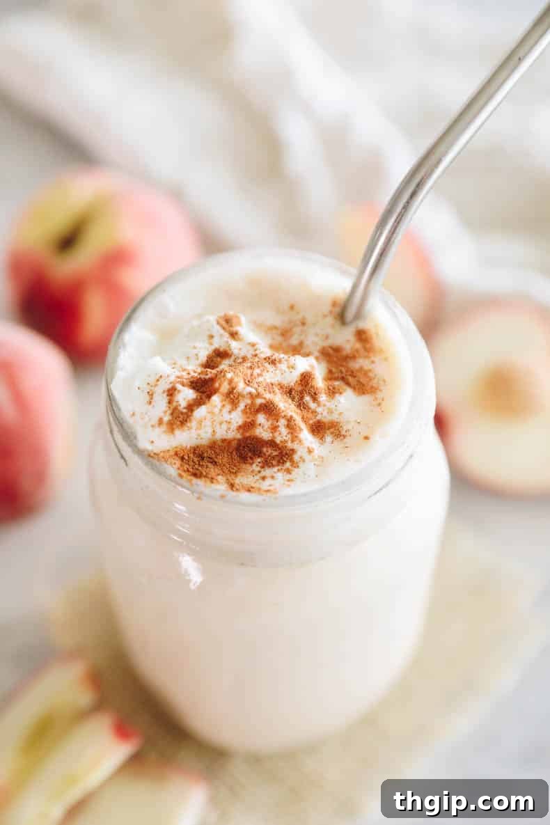 A perfectly blended peach smoothie in a mason jar, elegantly topped with a dash of cinnamon, ready for a refreshing sip.