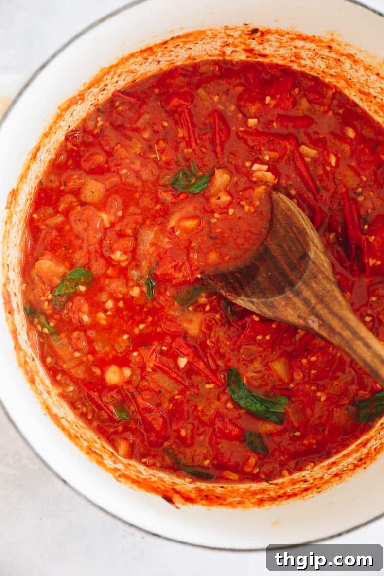 Slow Simmered Tomato Sauce 5 Rich homemade tomato sauce simmering gently in a large Dutch oven, with vibrant green basil leaves stirred in, promising deep flavors.