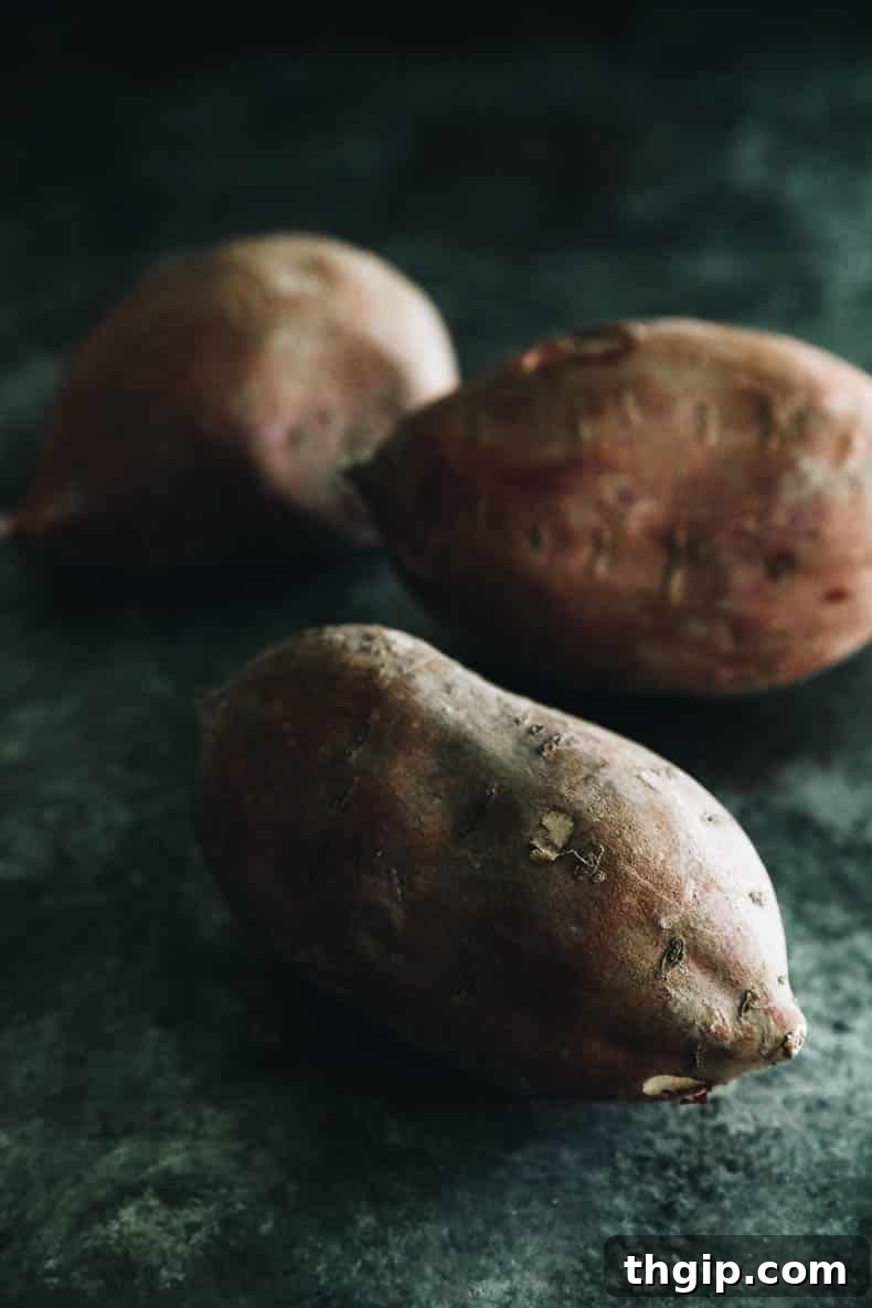 Sweet & Creamy Roasted Japanese Sweet Potato 3 Three unpeeled Japanese sweet potatoes on a kitchen countertop, showcasing their reddish-purple skin.
