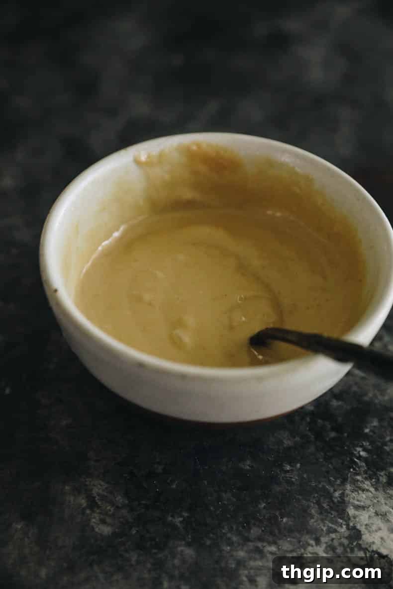 Sweet & Creamy Roasted Japanese Sweet Potato 5 A small white bowl filled with a creamy, light brown miso tahini sauce, ready to be drizzled.